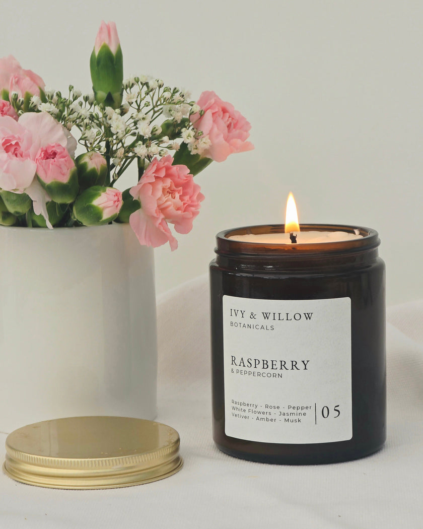 Black candle labeled 'Ivy & Willow' with a bouquet of pink flowers on a light background