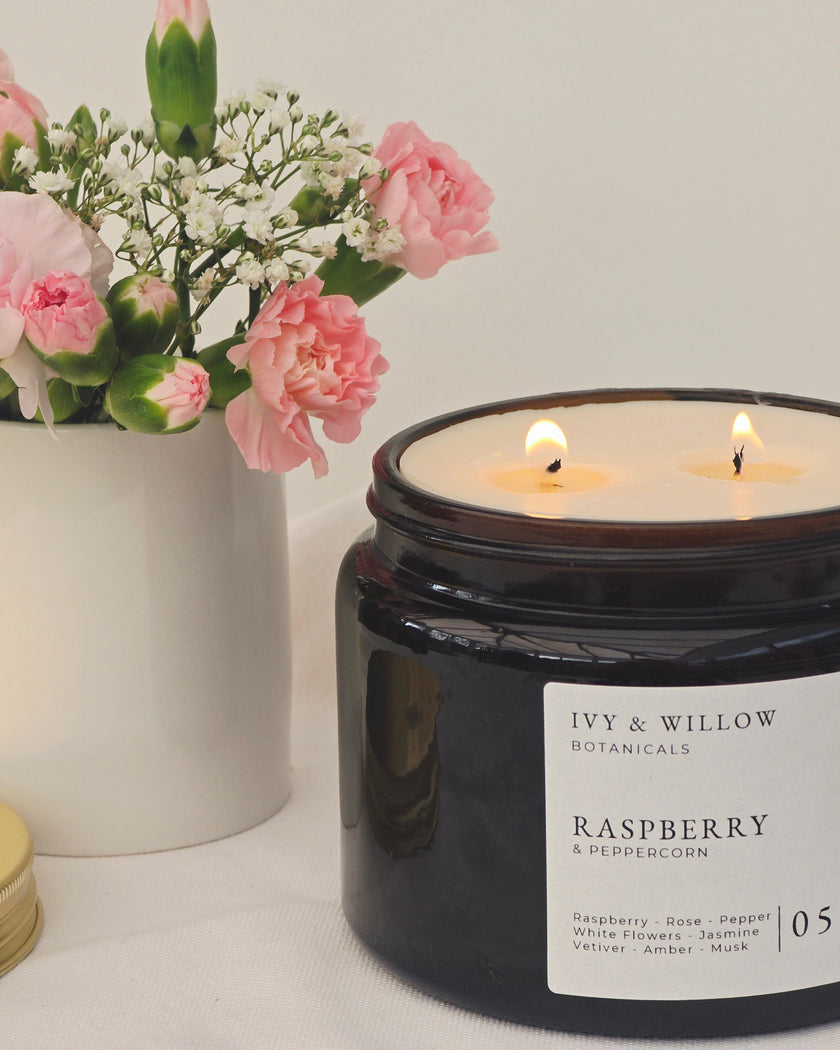Black candle jar with 'Ivy & Willow Botanicals' label next to a vase of pink flowers on a light background