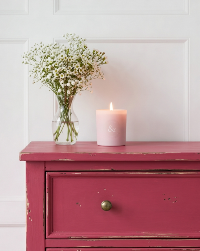 Pink dresser with a candle and vase of flowers on a white paneled wall