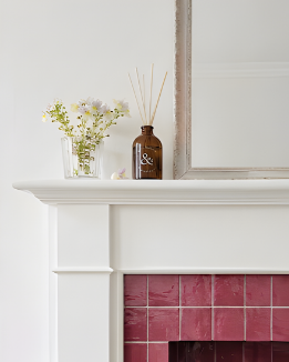 White fireplace with pink tiles, decorative vase, and flowers on a white mantel.