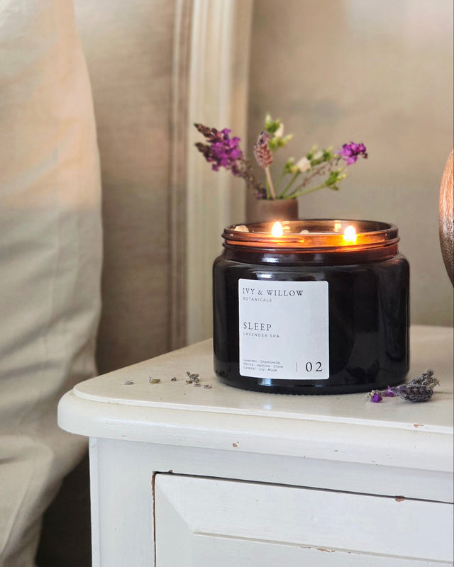 Candle on a nightstand next to a bed with decorative pillows