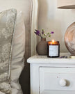 Candle on a nightstand next to a chair with decorative pillows and a globe.