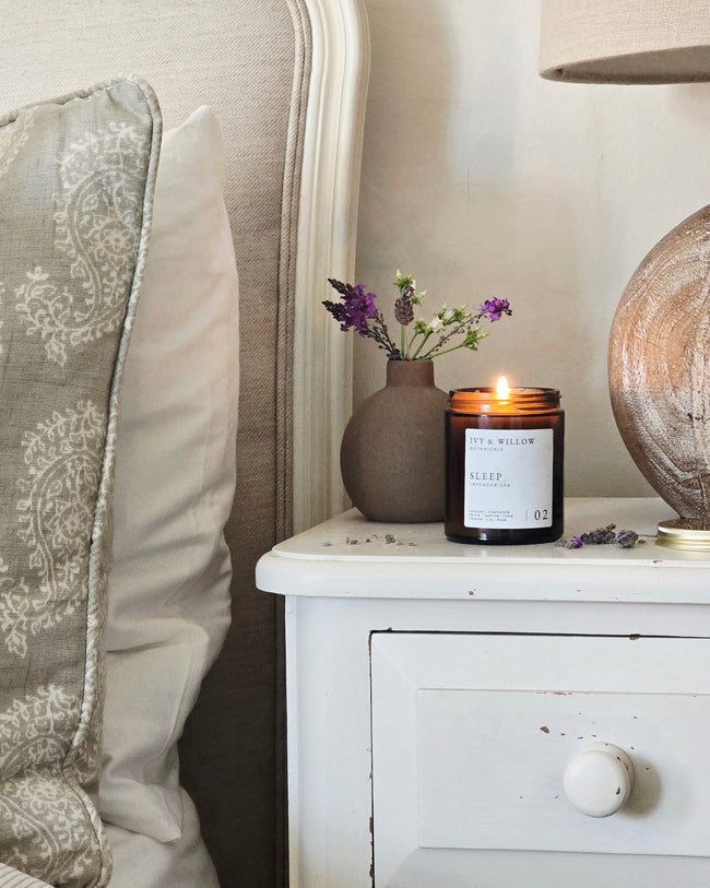 Candle on a nightstand next to a chair with decorative pillows and a globe.