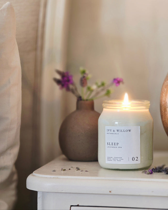 Candle labeled 'Sleep' on a nightstand with a vase of flowers in the background