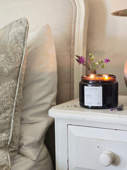 Candle on a nightstand next to a bed with decorative pillows