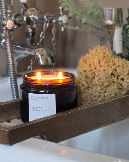 Candle in a black container labeled 'Ivy & Willow' on a bathroom shelf with a sponge and faucet in the background.