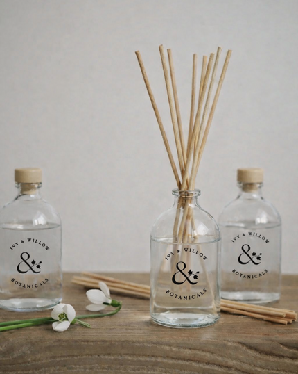 Two diffuser bottles with reeds and a flower on a wooden surface, branded 'Wilsor & Wilton Botanicals'.