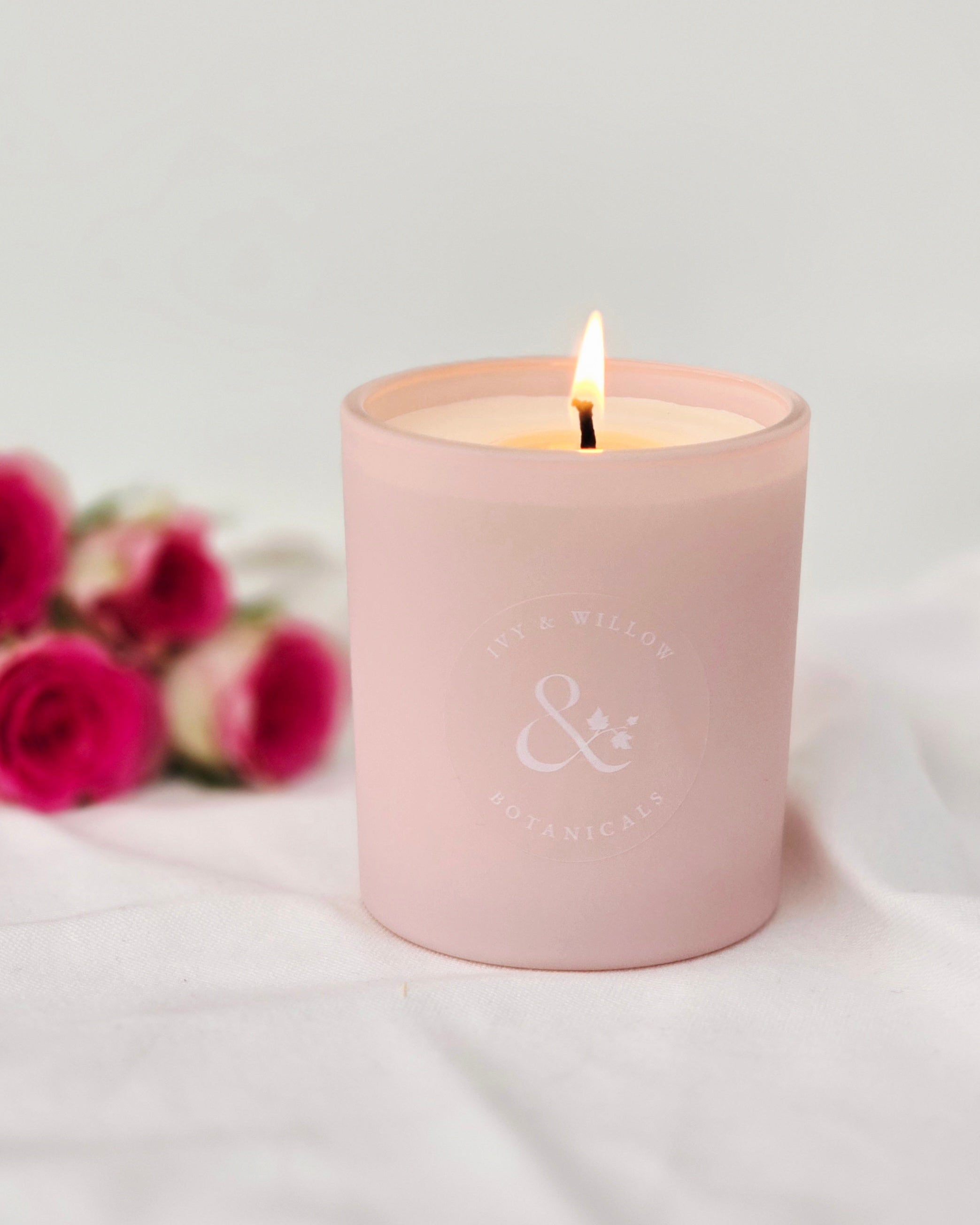 Pink candle with a logo on a white surface with pink flowers in the background