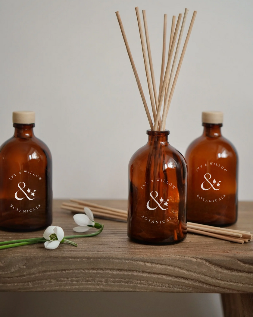 Three amber glass bottles with reeds and floral elements on a wooden surface, featuring 'My Willow Botanics' branding.