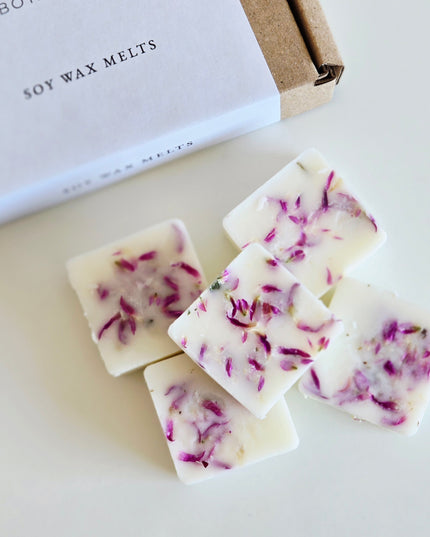 Soy wax melts with purple specks on a white surface, next to a box labeled 'Soy Wax Melts'.