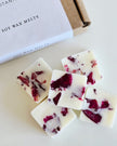 Soy wax melts with red flower petals on a white surface, next to a box labeled 'Soy Wax Melts'.