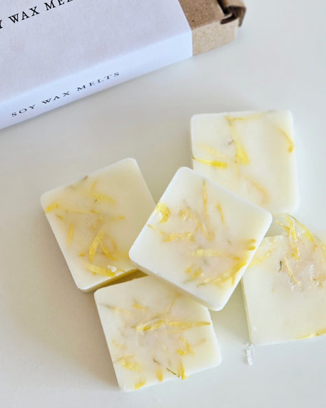 Soy wax melts with lemon zest on a white surface, with a box labeled 'Soy Wax Melts' in the background.