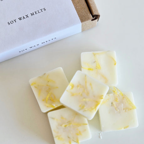 Soy wax melts with lemon zest on a white surface next to a box labeled 'Soy Wax Melts'.