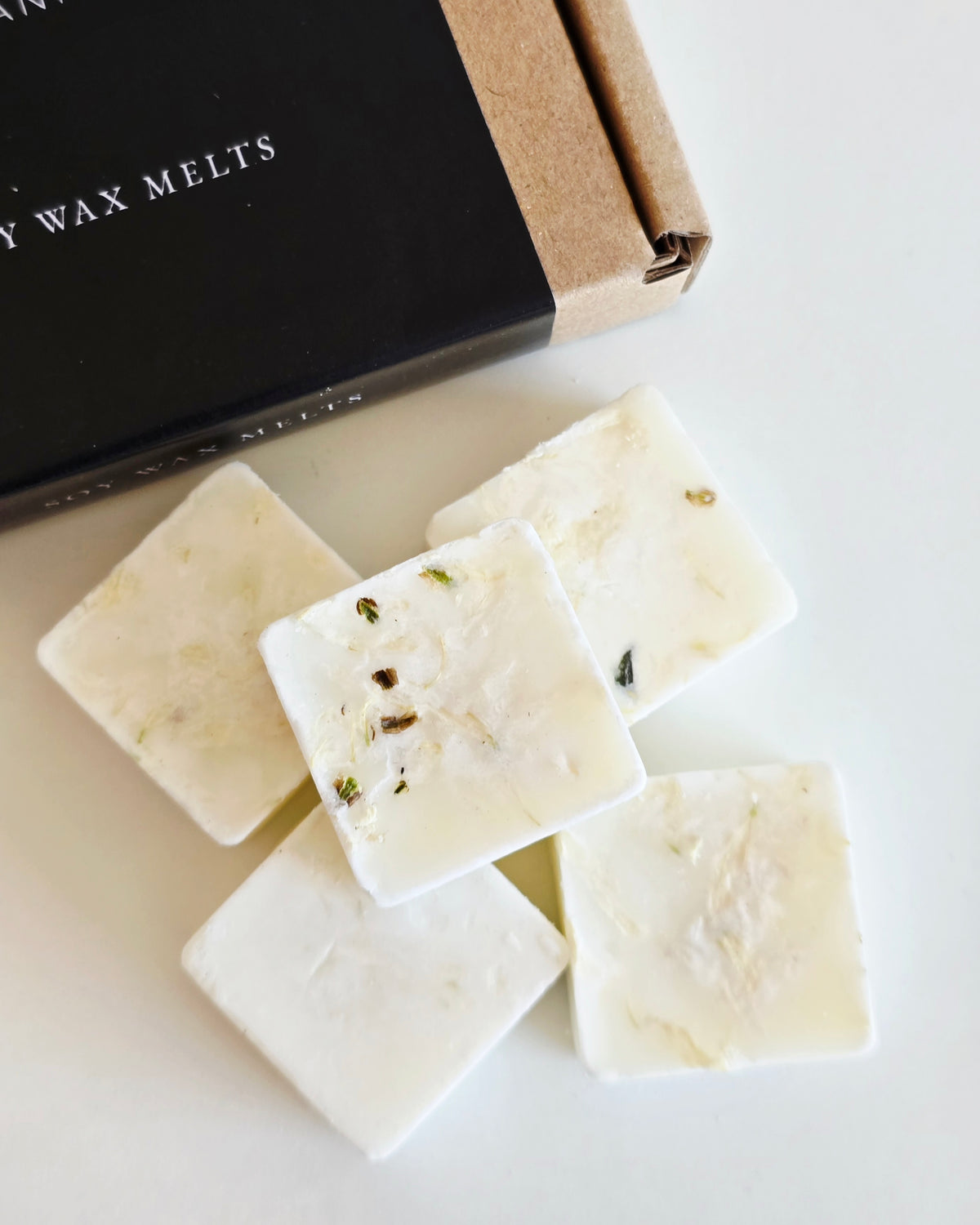 White wax melts with visible herbs on a white surface, next to a black box labeled 'Wax Melts'.