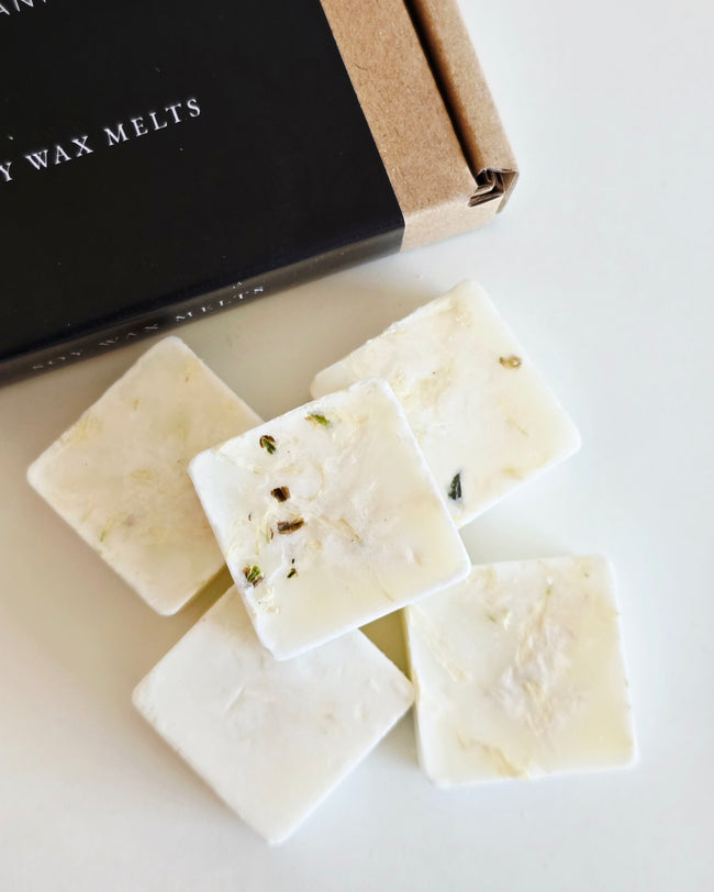 White wax melts with visible herbs on a white surface, next to a black box labeled 'Wax Melts'.