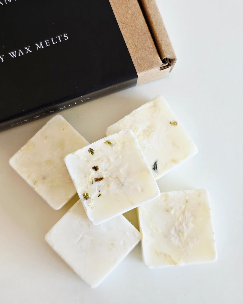 White wax melts with visible herbs on a white surface, next to a black box labeled 'Wax Melts'.