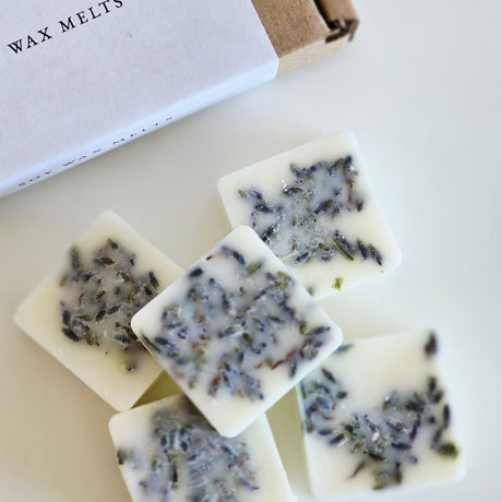 Wax melts with visible herbs on a white surface next to a box labeled 'Wax Melts'.