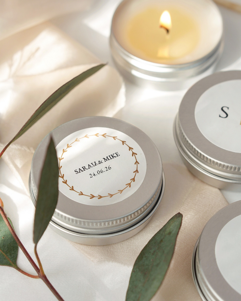 Silver tins with personalized labels and a lit candle on a light background