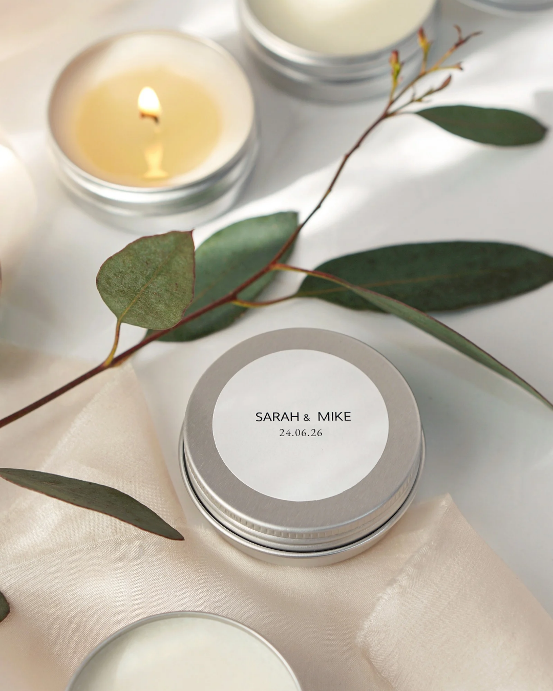Candle with a labeled tin and eucalyptus leaves on a light surface