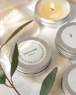 Silver tins with personalized labels and a lit candle on a light background
