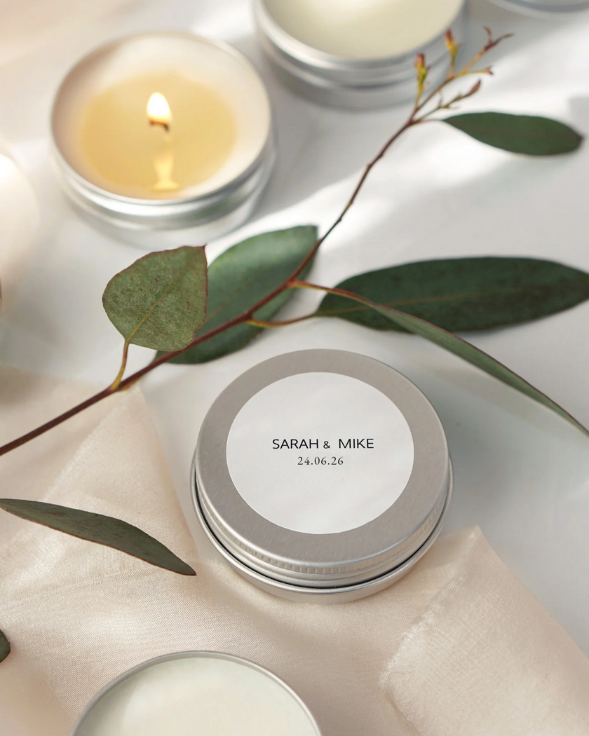 Candle with a labeled tin and eucalyptus leaves on a light surface