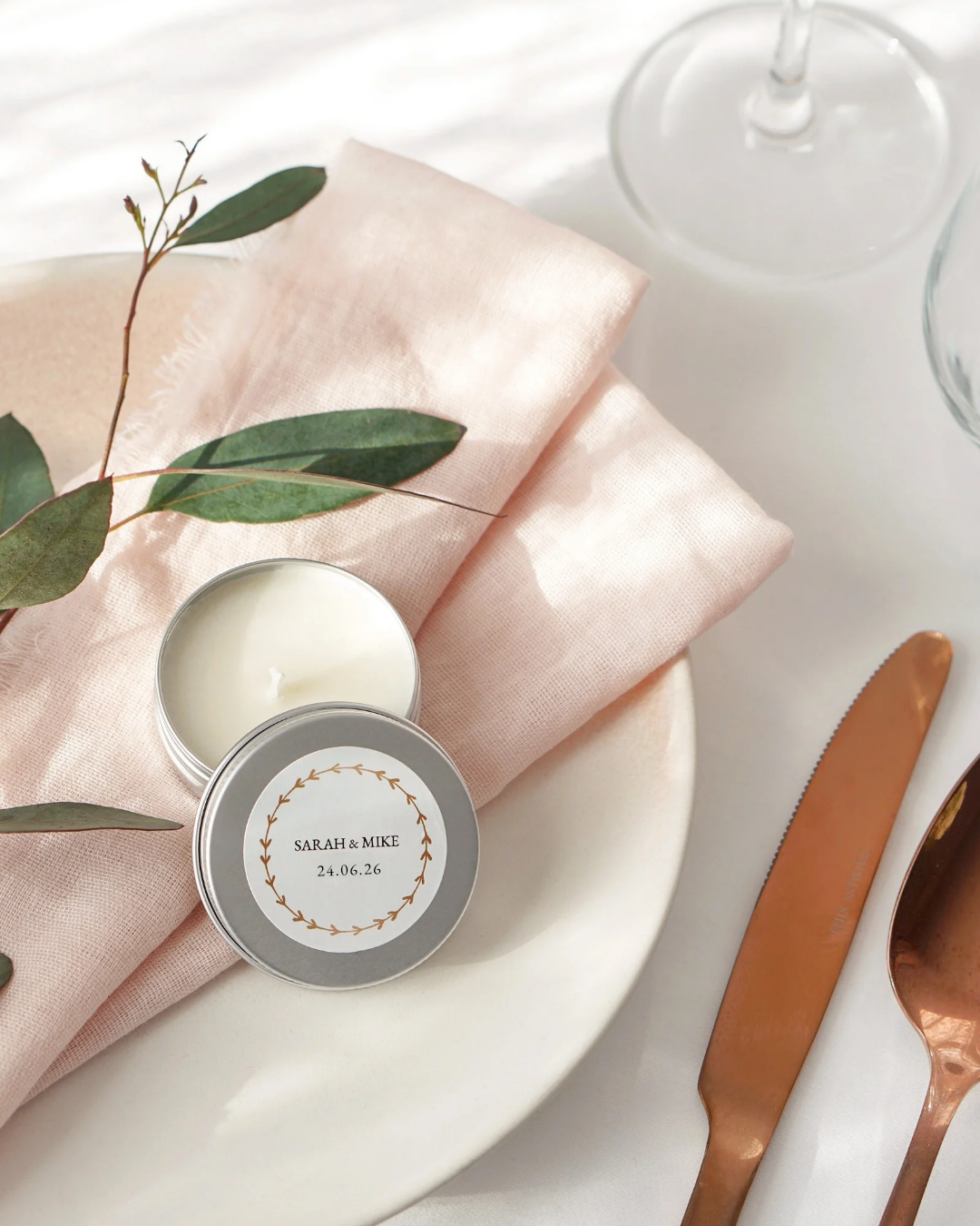 Small tin with a personalized label on a pink cloth with green leaves and a knife.