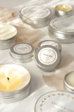 Silver tins with decorative labels and lit candles on a light background