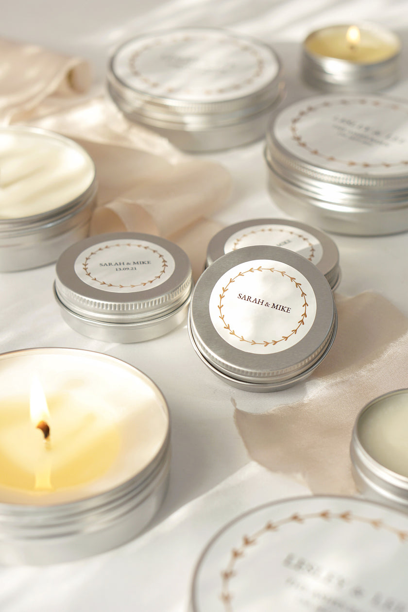 Silver tins with decorative labels and lit candles on a light background