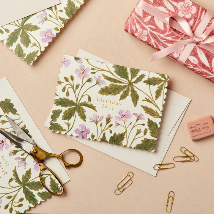 Floral card with 'birthday love' text on a beige surface with scissors and paper clips.