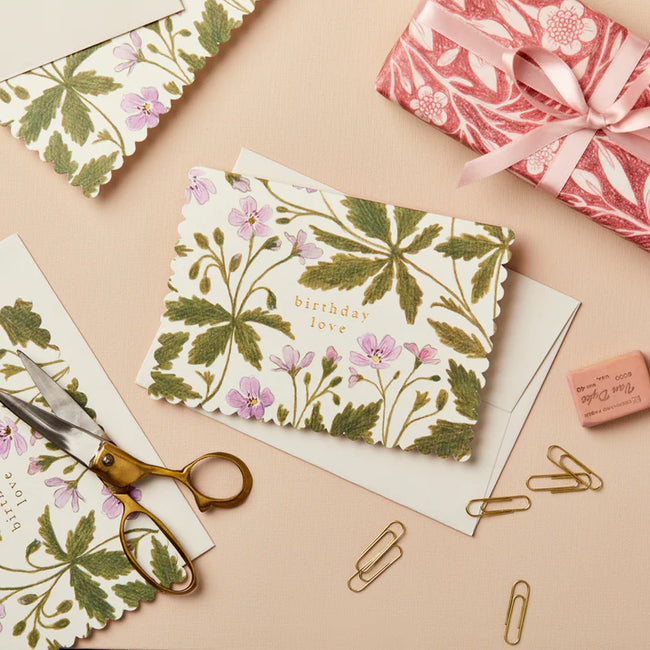 Floral card with 'birthday love' text on a beige surface with scissors and paper clips.