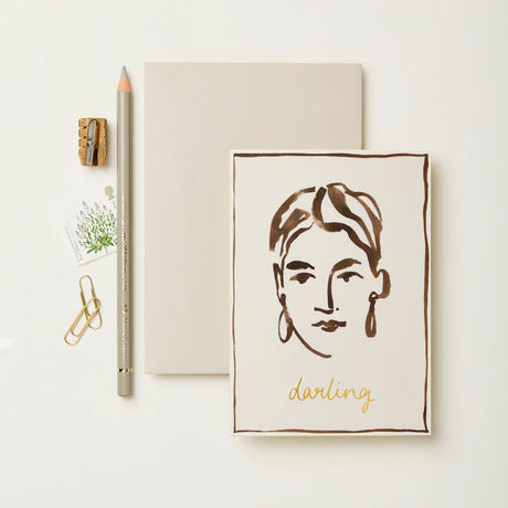 Notebook with a face illustration and 'darling' text, accompanied by stationery items on a light background.