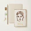 Notebook with a face illustration and 'darling' text, accompanied by stationery items on a light background.