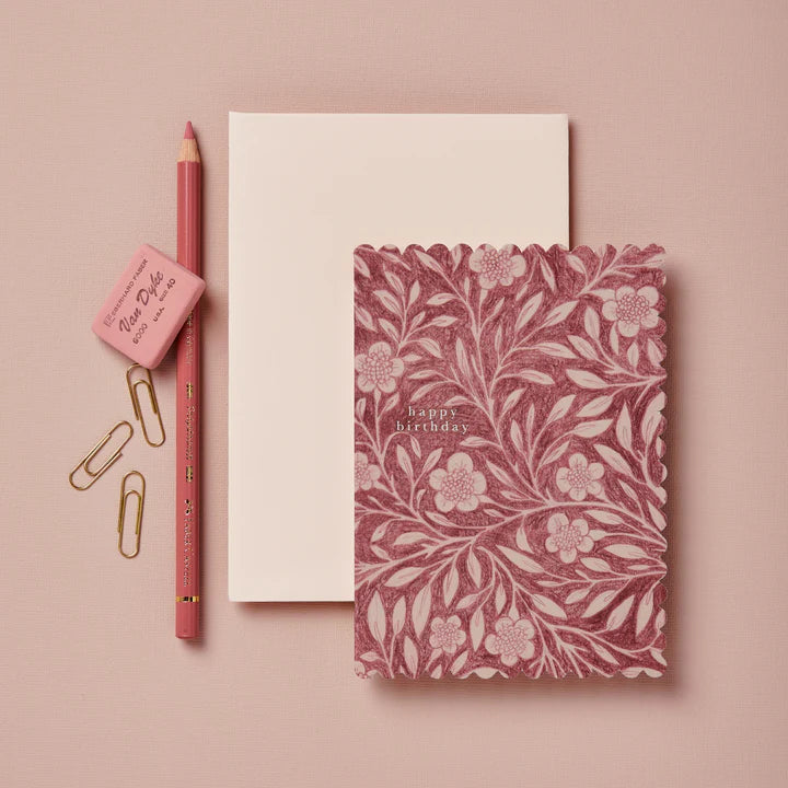 Notebook with floral design and 'Happy Birthday' text, pink pencil, eraser, and paper clips on a pink background