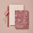 Notebook with floral design and 'Happy Birthday' text, pink pencil, eraser, and paper clips on a pink background