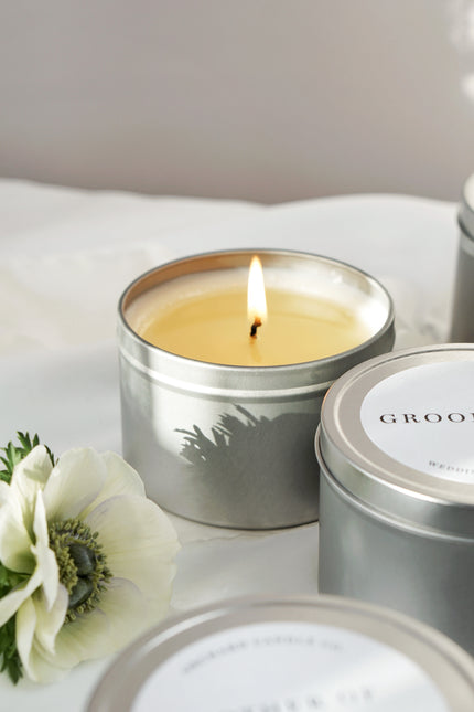 Candle in a metal tin with a white flower on a light surface