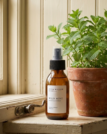 Bottle of 'Wild Mint & Eucalyptus' room spray next to a potted plant on a wooden surface.