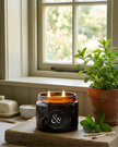 Candle in a black container with a plant on a windowsill