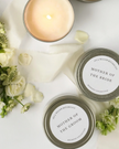 Two candles labeled 'Mother of the Bride' and 'Mother of the Groom' with floral elements on a white surface.