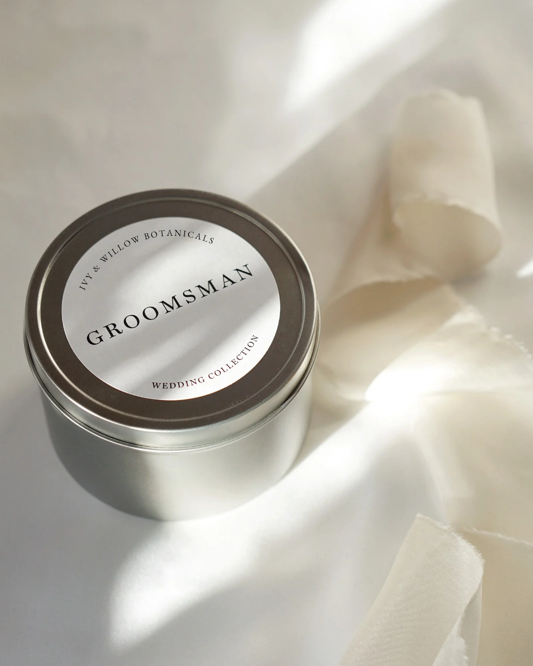 Silver tin labeled 'Groomsman' on a white fabric background